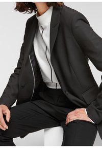 Svart blazer med snedkragar, enkel knapp och slim fit. Kombinerad med en vit tröja med hög krage och svarta detaljer.