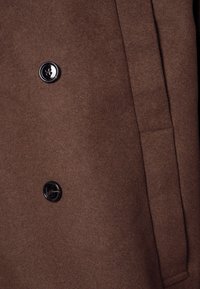 Brauner Wollmantel mit weicher Textur, doppelter Knopfleiste und glänzenden schwarzen Knöpfen. Mit Seitentaschen für zusätzliche Funktionalität.