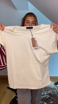 T-shirt creme de manga curta feito de algodão suave, com um decote redondo e uma etiqueta anexada, apresentando uma textura lisa e sem padrões.