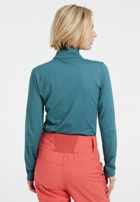 Maglia turchese a maniche lunghe con colletto alto, abbinata a pantaloni elasticizzati rosa chiaro con vita arricciata.