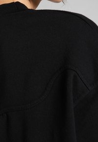 Acercamiento a una prenda de punto negra que muestra las costuras detalladas y la textura de la tela cerca del hombro y el escote.