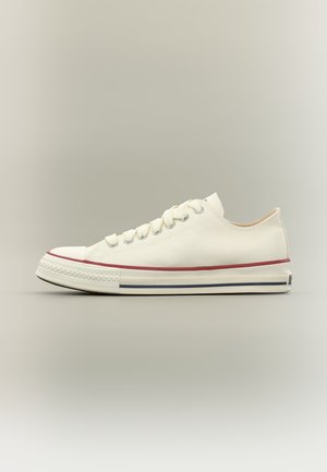 Sneaker bianco in tela con lacci bianchi, punta in gomma e suola con strisce rosse e blu.