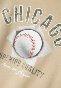 Una tela beis presenta un diseño gráfico con una pelota de béisbol rompiendo papel, rodeada del texto "CHICAGO" y "CALIDAD SUPERIOR".