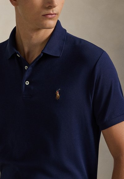 Mann trägt ein marineblaues Poloshirt mit einem kleinen gestickten Logo eines Polospielers zu Pferd auf der Brust.