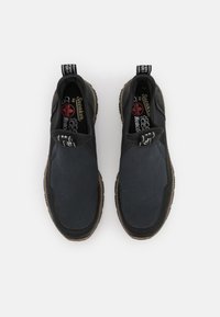 Zwarte instapsneakers van gestructureerde stof met gladde overlays, voorzien van een bruine rubberen zool en contrasterende trekbanden.