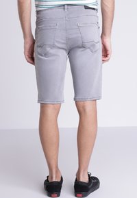 Pantalones cortos de mezclilla gris con un ajuste slim, que cuentan con bolsillos traseros y detalles de costura. Llevados con zapatillas negras y una camisa a rayas.