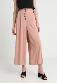 Light pink wide-leg trousers with a high waistband and five decorative buttons. Material appears soft with a smooth texture, suitable for warm weather.