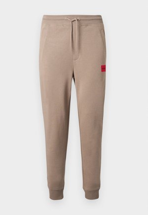Pantaloni jogger beige con vita elasticizzata e coulisse, tasche laterali, polsini a coste e una piccola toppa rettangolare rossa sul coscia.