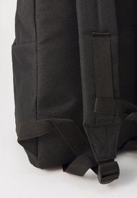 Mochila preta de tecido com material durável, alças ajustáveis, bolso lateral e uma fivela de plástico, apresentando uma superfície texturizada.