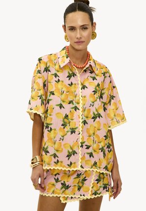 Chemise à manches courtes rose à fleurs avec imprimé citron jaune, bords festonnés et fermeture à boutons, assortie à une jupe mini.