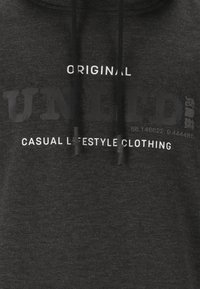 Grauer Hoodie mit Kängurutasche, Kordeln und fettem weißen Grafiktext. Das Material wirkt weich mit einer strukturierten Oberfläche.