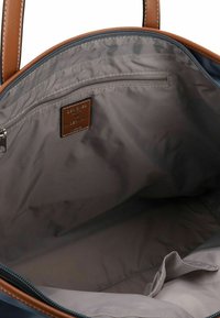 Interno di una borsa a tracolla blu navy con fodera grigia, dettagli in pelle, tasca con cerniera e design non strutturato. Presenta doppi manici marroni.