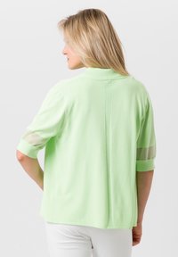 Mintgrünes T-Shirt mit kurzen Ärmeln in lockerer Passform, das durchsichtige Akzente an den Ärmeln und ein Detail an der rückseitigen Naht aufweist. Weicher Stoff.
