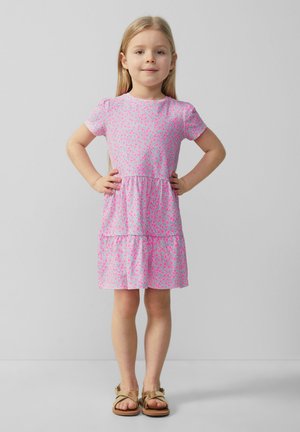 Robe rose à manches courtes avec un motif floral, jupe à volants, tissu doux, encolure ronde, associée à des sandales marron.