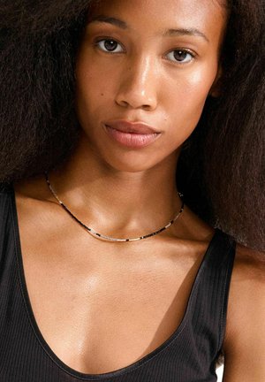 Kaelakee mustades, hõbedastes ja kullatoonides helmestega, millel on peen kujundus eri kujunditega ning tagasihoidlik, minimalistlik esteetika.