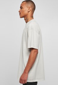 Lys grå oversized t-skjorte med rund hals, korte ermer og slitte detaljer på skuldrene. Myk bomullsstoff.