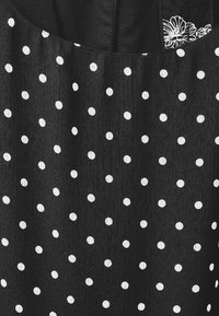 Svart tyg med vita prickar, med en texturerad yta och en fin blommig broderidetalj nära halsringningen.