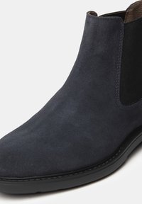 Bottines Chelsea en suède marine, présentant des panneaux latéraux élastiques, un bout arrondi et une surface texturée, reposant sur une semelle en caoutchouc noir solide.