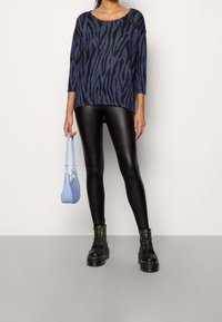 Blå och svart zebra-mönstrad topp med trekvartslång ärm, ihop med svarta fusk läder leggings och svarta snörkängor, håller en ljusblå väska.