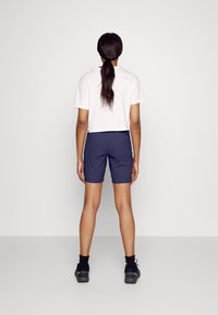 Kappad vit t-shirt och marinblå shorts. Outfiten har en avslappnad passform, med mjukt tyg och en logodetalj på baksidan av t-shirten.