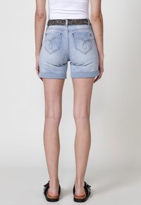Shorts en denim bleu clair avec des revers, présentant une taille décorative noire et colorée avec un motif et deux poches au dos.