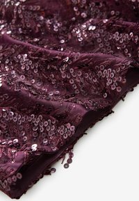 Tissu bordeaux avec des sequins cousus et des franges, présentant une surface texturée et un aspect scintillant, plié dans une disposition en couches.