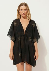 Svart, genomskinlig kimono-inspirerad kaftan med guldstjärntryck, djup V-hals, justerbar dragsko i midjan och vida ärmar.