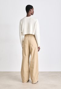 Pull en tricot blanc coupé associé à un pantalon cargo beige ample ; présente des poches appliquées et une taille haute, mettant en valeur une coupe décontractée.