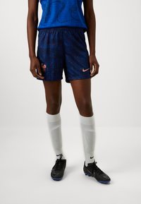 Nike football shorts in dark navy with red accents, featuring a rooster emblem and a subtle pattern. Paired with white knee-high socks and black cleats.