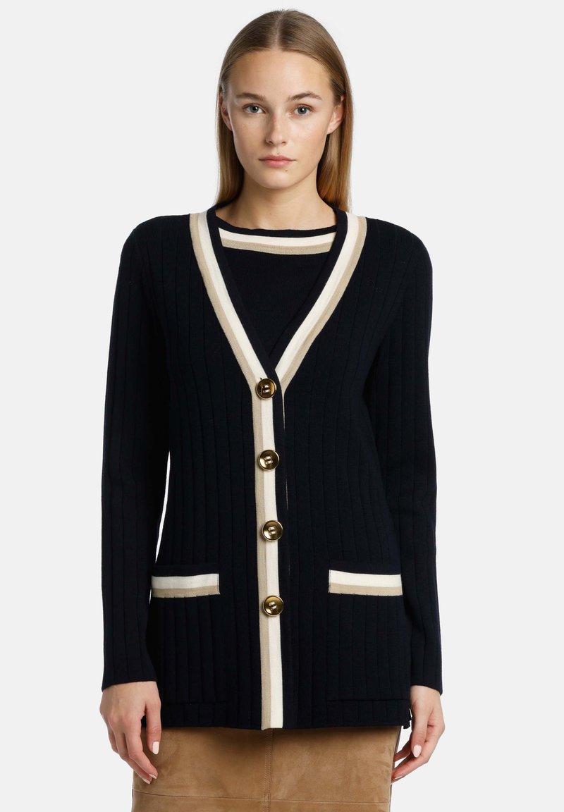 Marinblå cardigan med ribbad struktur, kontrasterande krämfärgade kanter och fyra guldknappar, med två framfickor med krämfärgade detaljer.