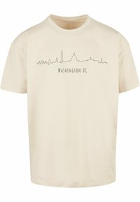 Tricou crem din bumbac, cu un grafic minimalist al orizontului gri al Washington, D.C., având textul "WASHINGTON DC" dedesubt.