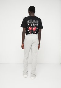 Schwarzes Grafik-T-Shirt mit rotem Herzdesign und weißem Text, kombiniert mit hellgrauen Sweatpants. Aus Baumwollmaterial, lockere Passform und lässiger Stil.