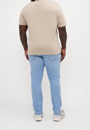Beige short-sleeve t-shirt with a round neckline, paired with light blue jeans. The outfit is completed with gray athletic shoes.