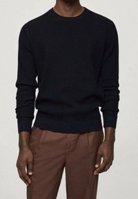 Námořnický žebrovaný pletený svetr s kulatým výstřihem a dlouhými rukávy, s přiléhavým lemem. Nosen s hnědými kalhotami.