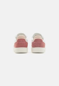 Ett par vita sneakers med rosa mockapaneler på hälen och "Calvin Klein Jeans" präglat på ljusrosa hälflikarna, visade från baksidan.