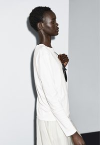 Hvid langærmet top med rund halsudskæring, kombineret med et let, flydende skørt. Glat tekstur, rene linjer og minimalistisk design.