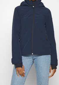 Námořnický modrý skládaný pásek z lehkého materiálu, s předním zipem, bočními kapsami a manžetami s otvory pro palce.