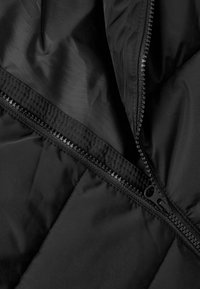 Interno di un giubbotto a vento nero con texture in nylon liscia, cerniera visibile e dettagli in cucitura trapuntata.