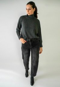Pull à col roulé tricoté gris avec des détails en côtes, associé à un jean noir taille haute et des bottines, sur un fond neutre.