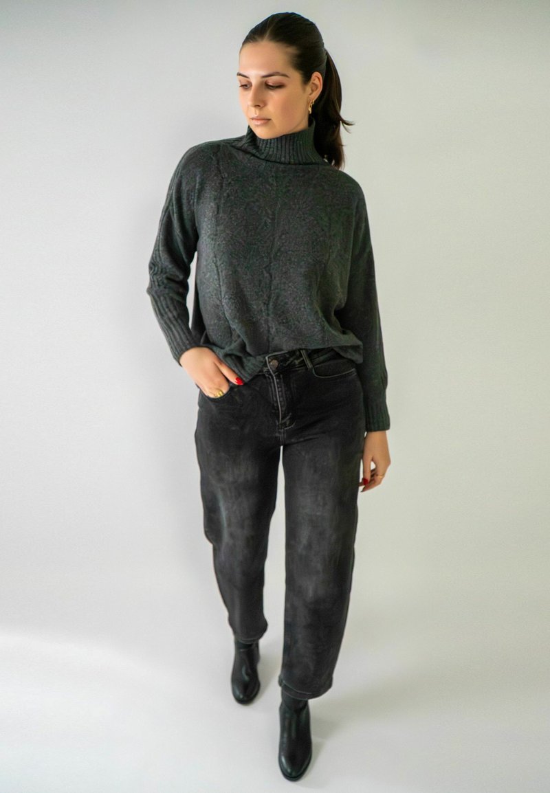Pull à col roulé tricoté gris avec des détails en côtes, associé à un jean noir taille haute et des bottines, sur un fond neutre.