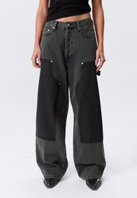 Τζιν με φαρδύ πόδι σε σκούρο γκρι denim με μαύρες λεπτομέρειες σε πάτσες στις εμπρόσθιες τσέπες και τους γοφούς. Διαθέτουν ασημένια εξαρτήματα και ψηλή μέση.