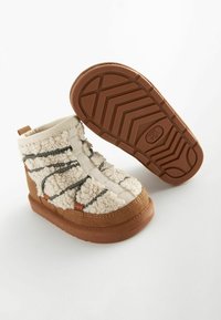 Stivaletti alla caviglia in suede tan con parte superiore in fleece crema testurizzato, dotati di cinturini elastici neri e suola in gomma con motivo.