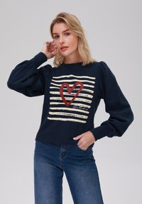 Sweatshirt marine avec un graphique de cœur crème et rouge entouré de lignes de coups de pinceau horizontales ; coupe décontractée avec des manches bouffantes ; en mélange de coton.