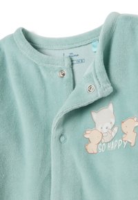 Mono de felpa verde menta con botones a presión, que presenta un mapache de dibujos animados y conejos, y el texto "SO HAPPY" impreso debajo del diseño.