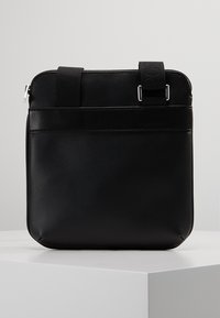 Borsa a tracolla in pelle nera con una texture liscia. Presenta una chiusura con zip, una tracolla regolabile e una tasca frontale con un pannello orizzontale.