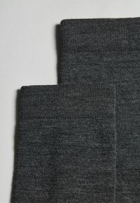 Calzini grigi a maglia con polsini a coste, caratterizzati da una texture morbida e da un motivo uniforme, piegati per mostrare due diverse altezze dei polsini.