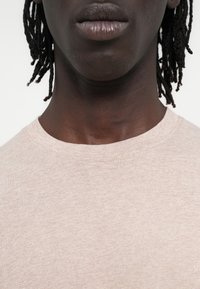 Majica s kratkimi rokavi iz svetlo roza bombaža z okroglim izrezom. Teksturirana tkanina in subtilen pikčast vzorec ustvarjata vizualno zanimivost.