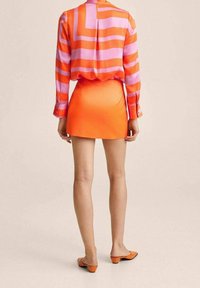 Chemise à manches longues à rayures horizontales roses et orange, associée à une mini-jupe orange vif et des chaussures orange sans lacets.