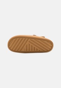 Gummisåle med en strukturert overflate med ribber og spor, hovedsakelig i en tan-farge, designet for grep og holdbarhet.