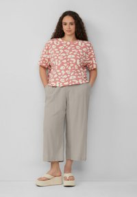 Rosa Hemd mit weißem Leopardenmuster, lockere Passform. Hellgraue Weitbeine-Hosen und beiger Plateau-Sandalen vervollständigen das Outfit.